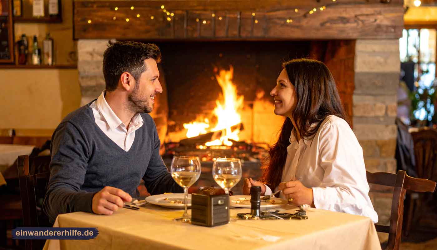Kecskemet vibes? Ein Paar sitzt in einem ungarischen Restaurant am Kaminfeuer, genießt ein Abendessen mit Wein und lächelt sich an.